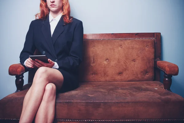 Businesswoman sitting on sofa reading on tablet — Stock Photo, Image