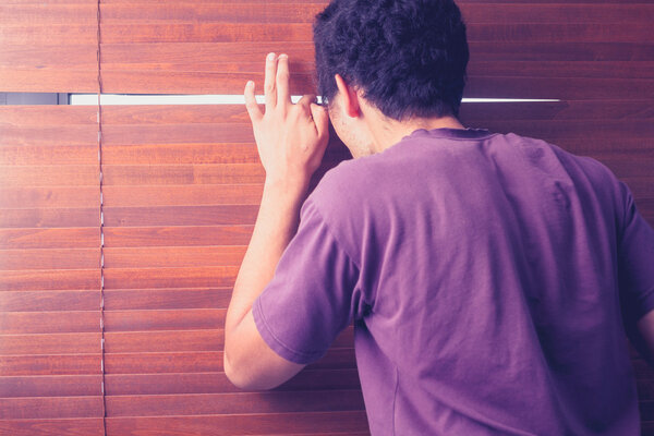 Молодой человек подглядывает сквозь жалюзи
