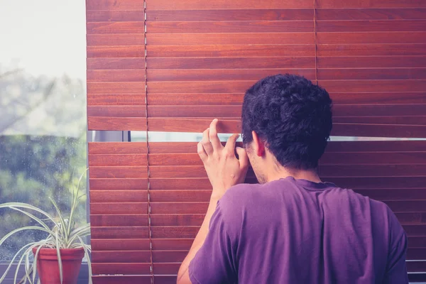 Jovem a espreitar através de cortinas venezianas — Fotografia de Stock