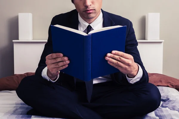 Serious young businessman sitting in bed reading book — Stock Photo, Image