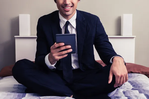 Feliz joven empresario sentado en la cama leyendo en la tableta — Foto de Stock