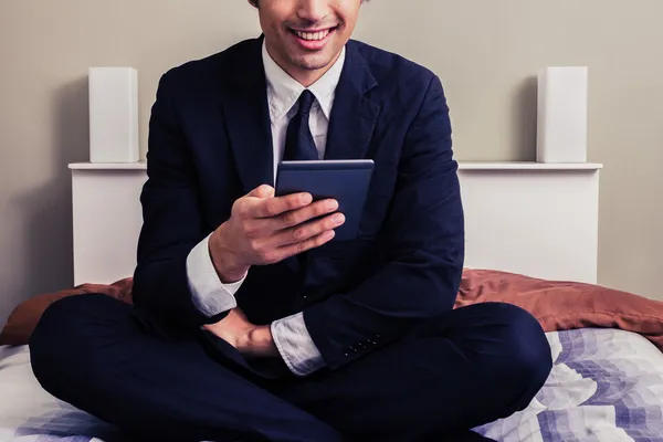 Jovem empresário feliz sentado na cama lendo no tablet — Fotografia de Stock