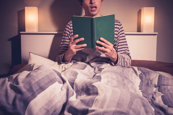 Young man is reading in bed — Stock Photo, Image