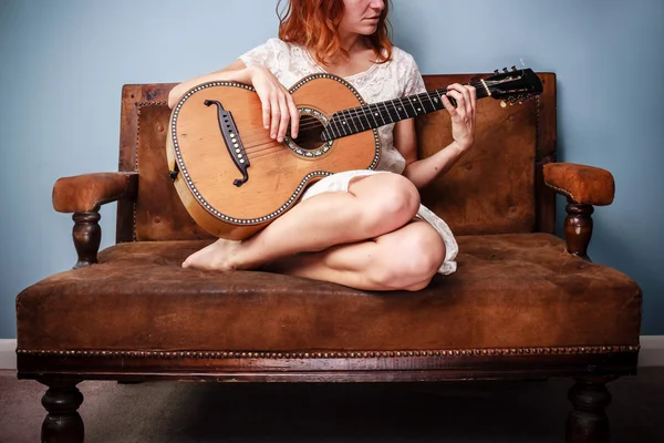 Mulher bonita no sofá está tocando guitarra — Fotografia de Stock