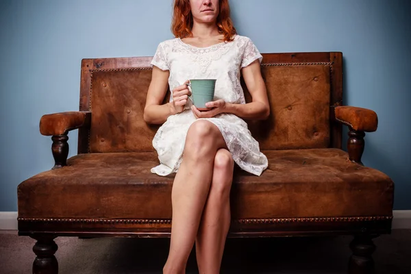 Jovem mulher no vestido de verão sentado no velho sofá bebendo chá — Fotografia de Stock