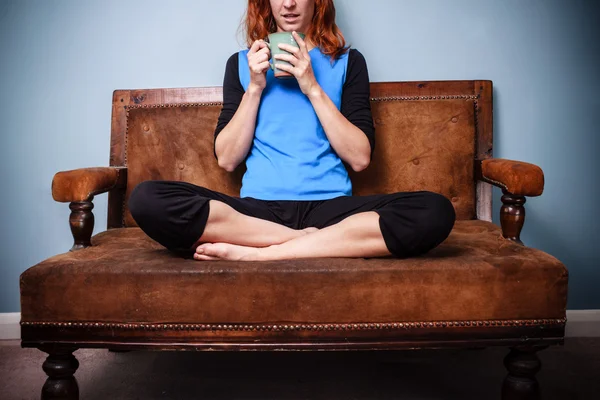 Junge Frau in lockerer Pose trinkt Tee auf altem Sofa — Stockfoto