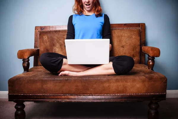 Glückliche junge Frau sitzt auf einem Sofa und benutzt ihren Laptop — Stockfoto