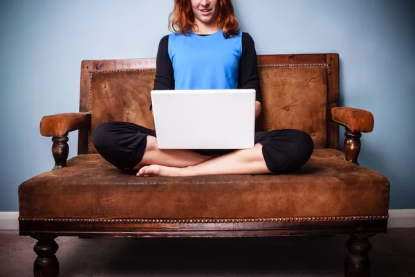 Mujer joven y tranquila sentado en el sofá con las piernas cruzadas con el ordenador portátil — Foto de Stock