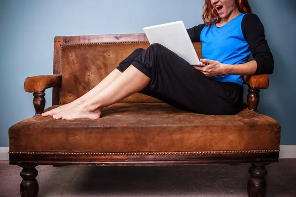 Happy young woman sitting on sofa using her laptop — Stock Photo, Image