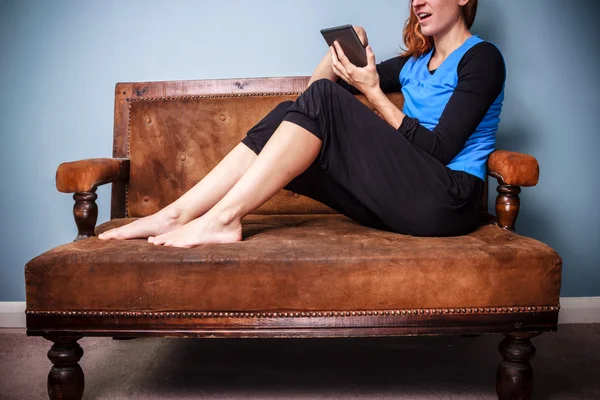 Ung kvinna sitter på soffa läser digital bok — Stockfoto