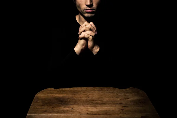 Человек молится в темноте за столом — стоковое фото