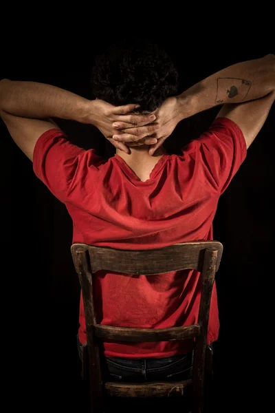 Young man sitting on old chair with hands behind head — Stock Photo, Image