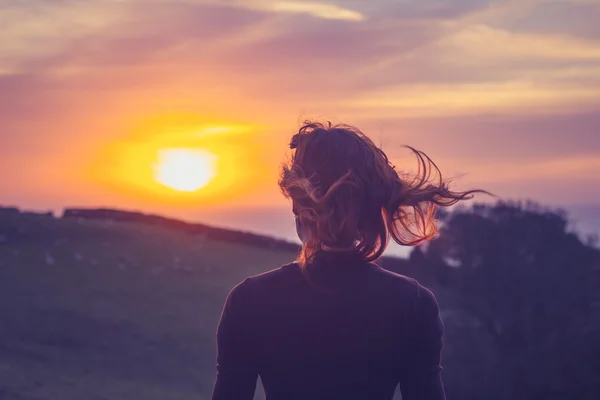 Mujer joven admirando la puesta de sol en los campos — Foto de Stock