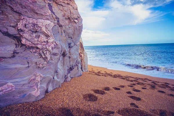 Impronte sulla spiaggia vicino a una scogliera — Foto Stock