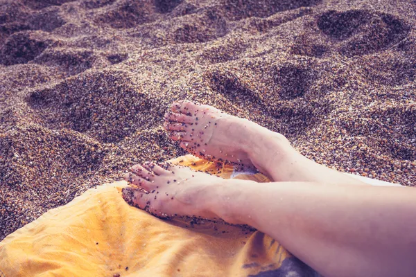 卵石海滩上躺着一名年轻女子的脚 — 图库照片