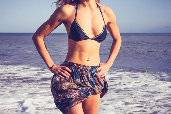 Jonge vrouw met afgetraind abs staande op het strand — Stockfoto