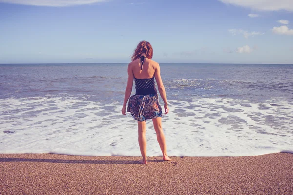 Bakifrån av ung kvinna som står på stranden och titta på havet — Stockfoto
