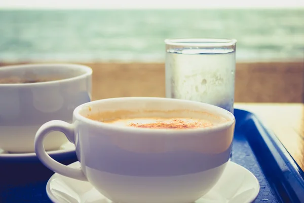 Cappucino en koffie op de lade door de zee — Stockfoto