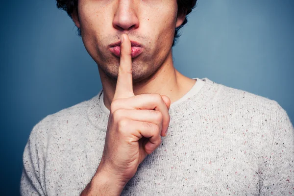 Young man gesturing hush with finger on lips — Stock Photo, Image