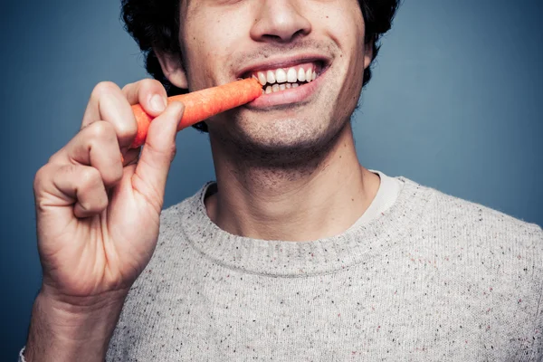 Jeune homme mangeant une carotte — Photo