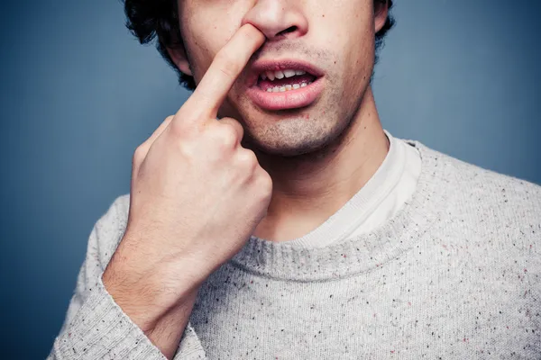 Jonge man is het oppakken van zijn neus — Stockfoto