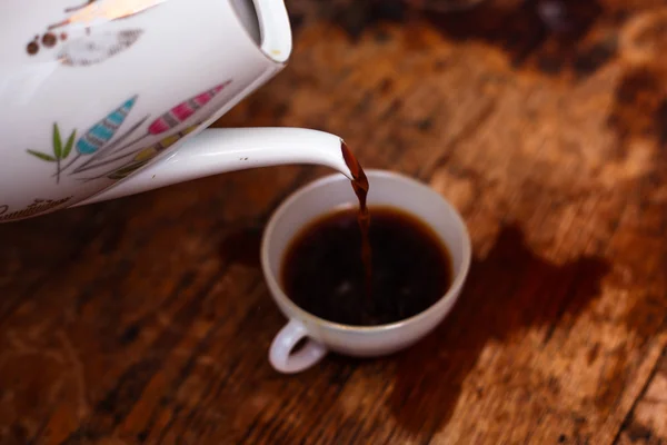 Café que se vierte en una taza de porcelana blanca sobre una mesa de madera — Foto de Stock