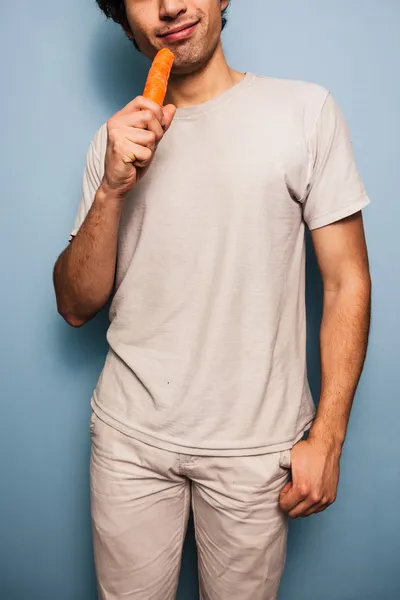 Happy young man eating a carrot — Stock Photo, Image