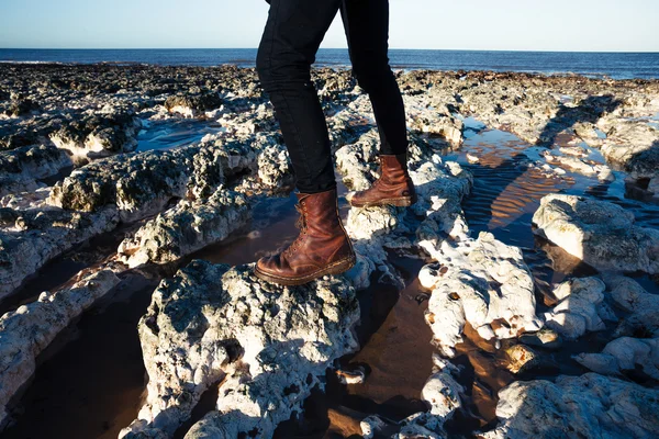 Närbild på stövlar promenader bland stenarna på stranden — Stockfoto