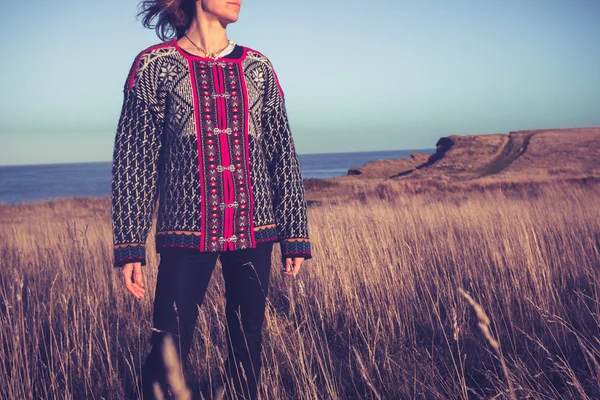 Mujer joven esperanzada de pie en el prado junto al mar al atardecer — Foto de Stock