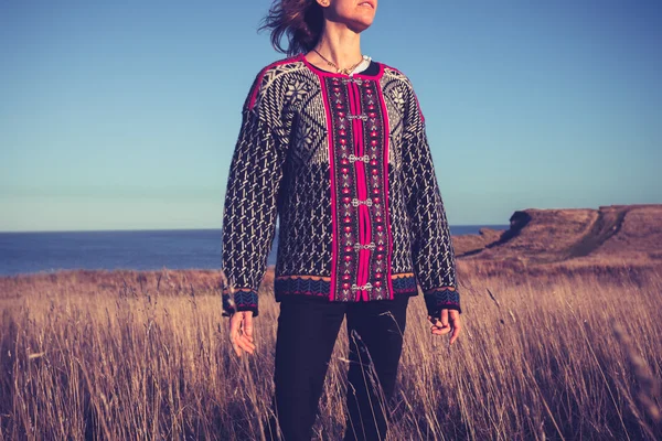Jovem esperançosa em pé no prado junto ao mar ao pôr do sol — Fotografia de Stock
