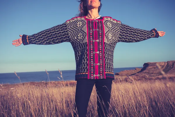 Young woman throwing her arms back in meadow by the sea — Stock Photo, Image