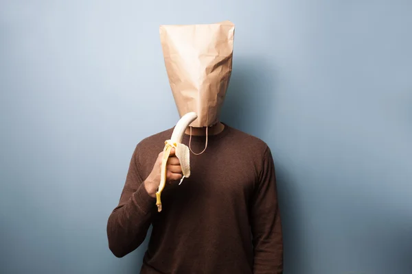Junger Mann mit Tasche über dem Kopf isst eine Banane — Stockfoto