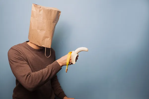 Young man with bag over his head using banana as gun — Stock Photo, Image