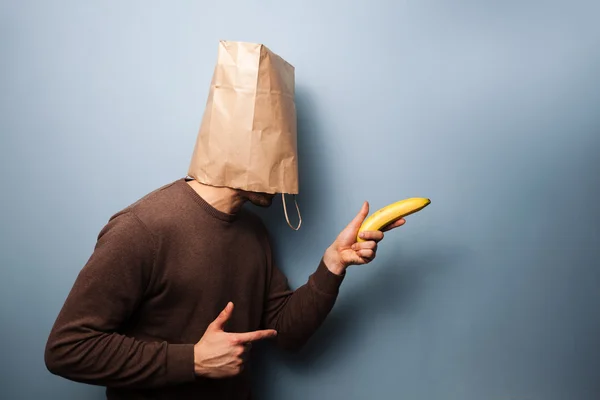 Young man with bag over his head using banana as gun — Stock Photo, Image