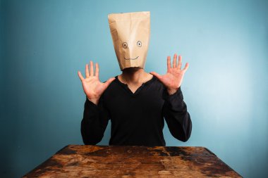 Stupid man with bag over his head and hands up clipart