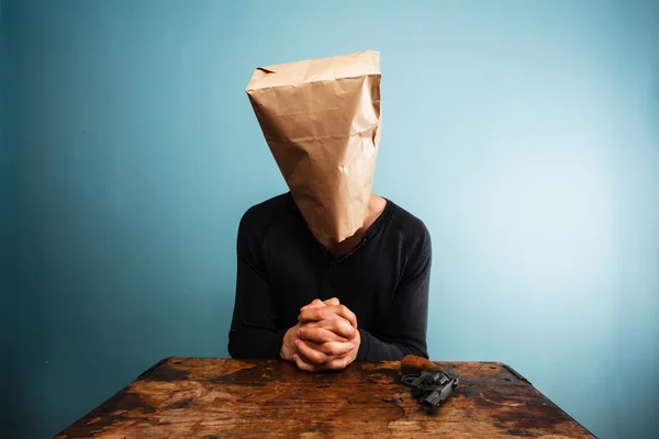 Man with revolver and a bag over his head is praying — Stock Photo, Image