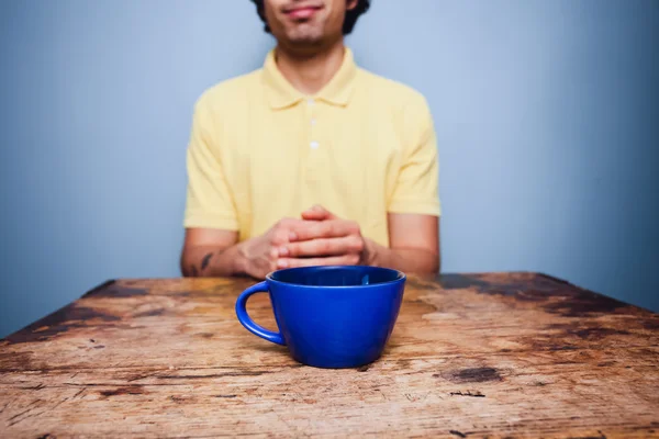 Jovem sentado à mesa com xícara de café — Fotografia de Stock