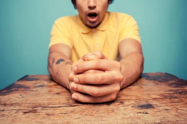 Jonge man met gevouwen handen op zoek geschrokken — Stockfoto