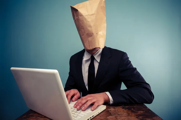 Empresario con bolsa sobre la cabeza trabajando en la computadora — Foto de Stock
