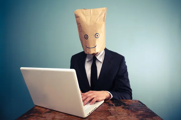 Businessman with bag over head working on computer — Stock Photo, Image