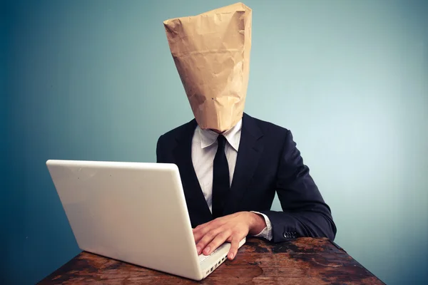Empresario con bolsa sobre la cabeza trabajando en la computadora — Foto de Stock