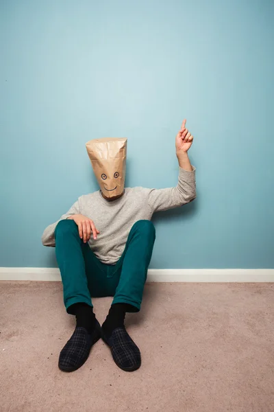 Man with bag over head on floor is pointing — Stock Photo, Image