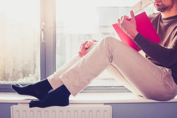 Junger Mann liest auf Fensterbank — Stockfoto