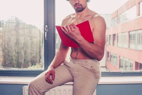 Sexy shirtless man leest door venster — Stockfoto