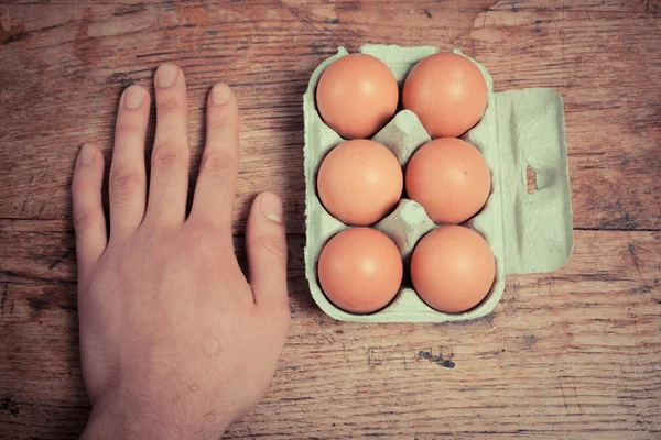 Main sur la table avec boîte d'œufs — Photo