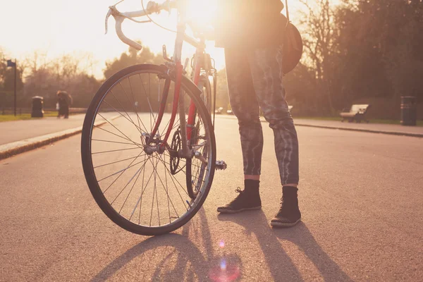 Jeune femme debout avec vélo au coucher du soleil — Photo