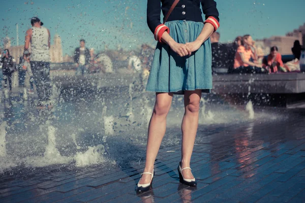 Mujer joven parada junto a la fuente en la ciudad en un día caluroso — Foto de Stock