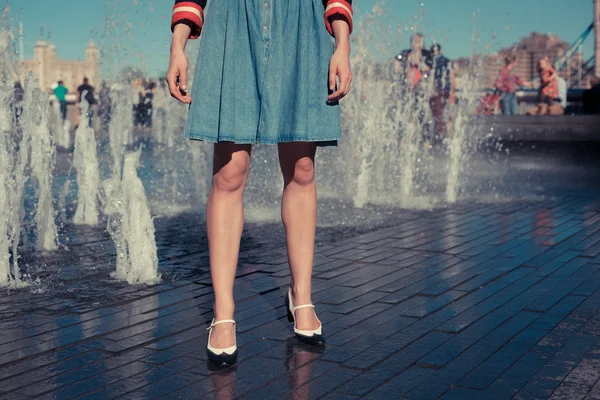 Mladá žena stojící u fontány v městě na horký den — Stock fotografie