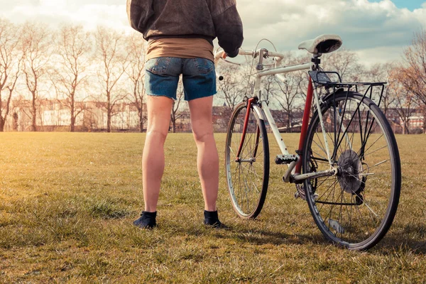 Ung kvinna som står i parken med cykel — Stockfoto