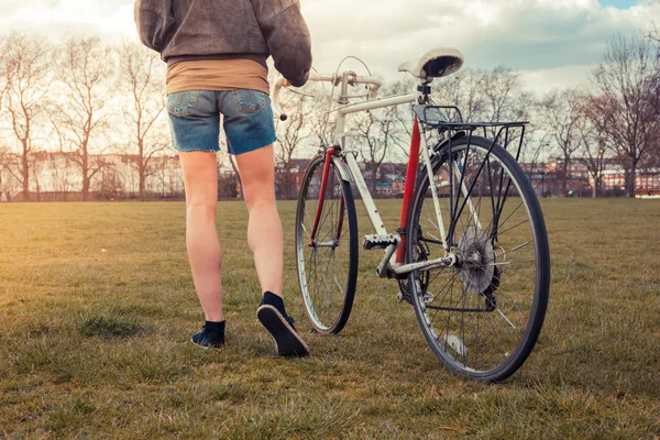 Ung kvinna vandring i parken med cykel — Stockfoto